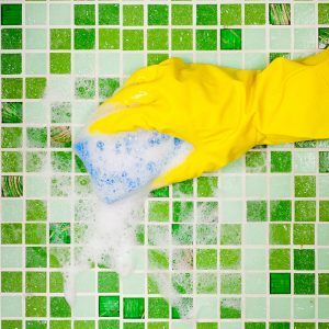 Person wearing rubber gloves scrubbing the tile with a sponge 