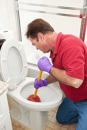 Man wearing gloves holding a plunger, plunging a toilet 