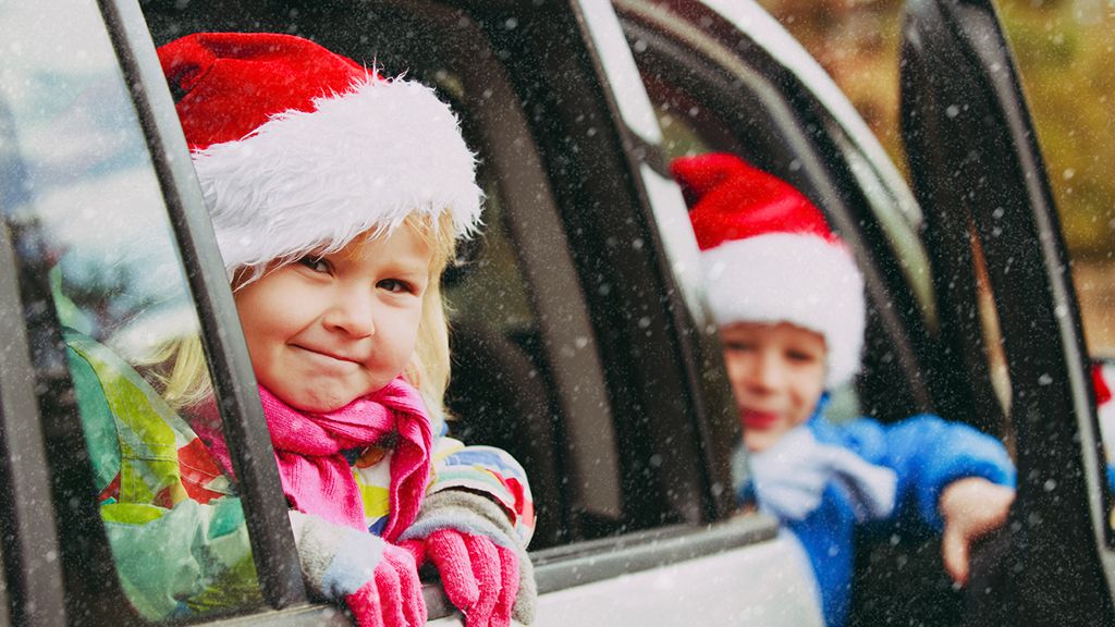 Two children sticking their heads outside of a car window wearing Santa hats 