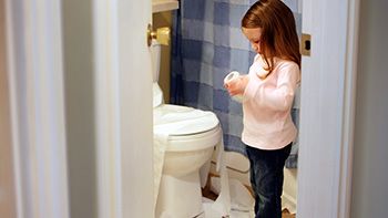 child standing next to a toilet holding a roll of toilet paper