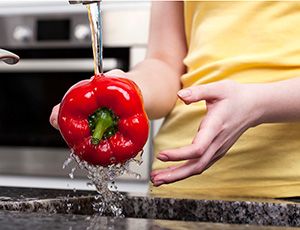 Person washing a red bell pepper under the sink